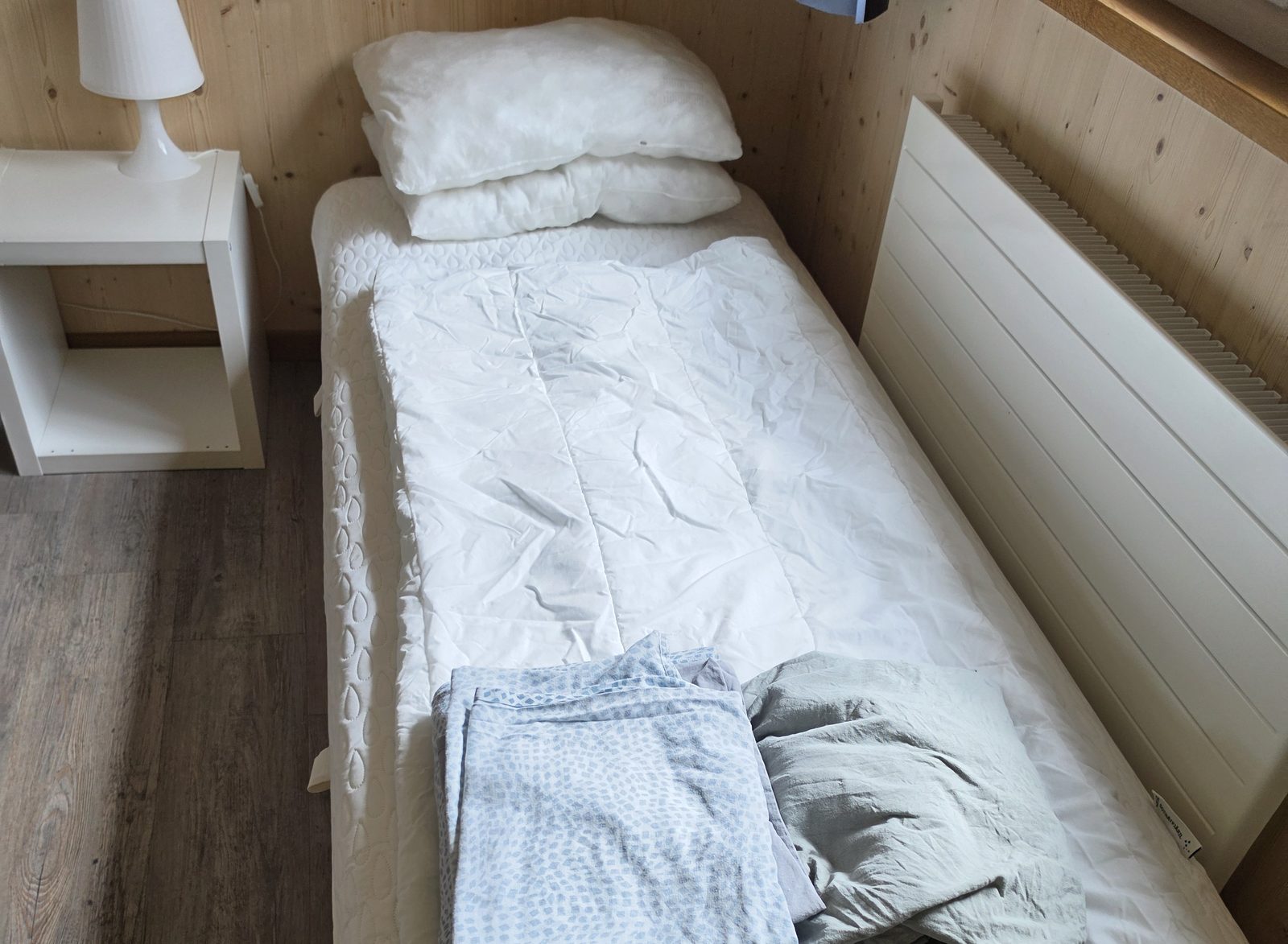 Frisch gewaschene, gefaltete Bettwäsche und Kissen bereitgestellt auf einem unbezogenen Bett