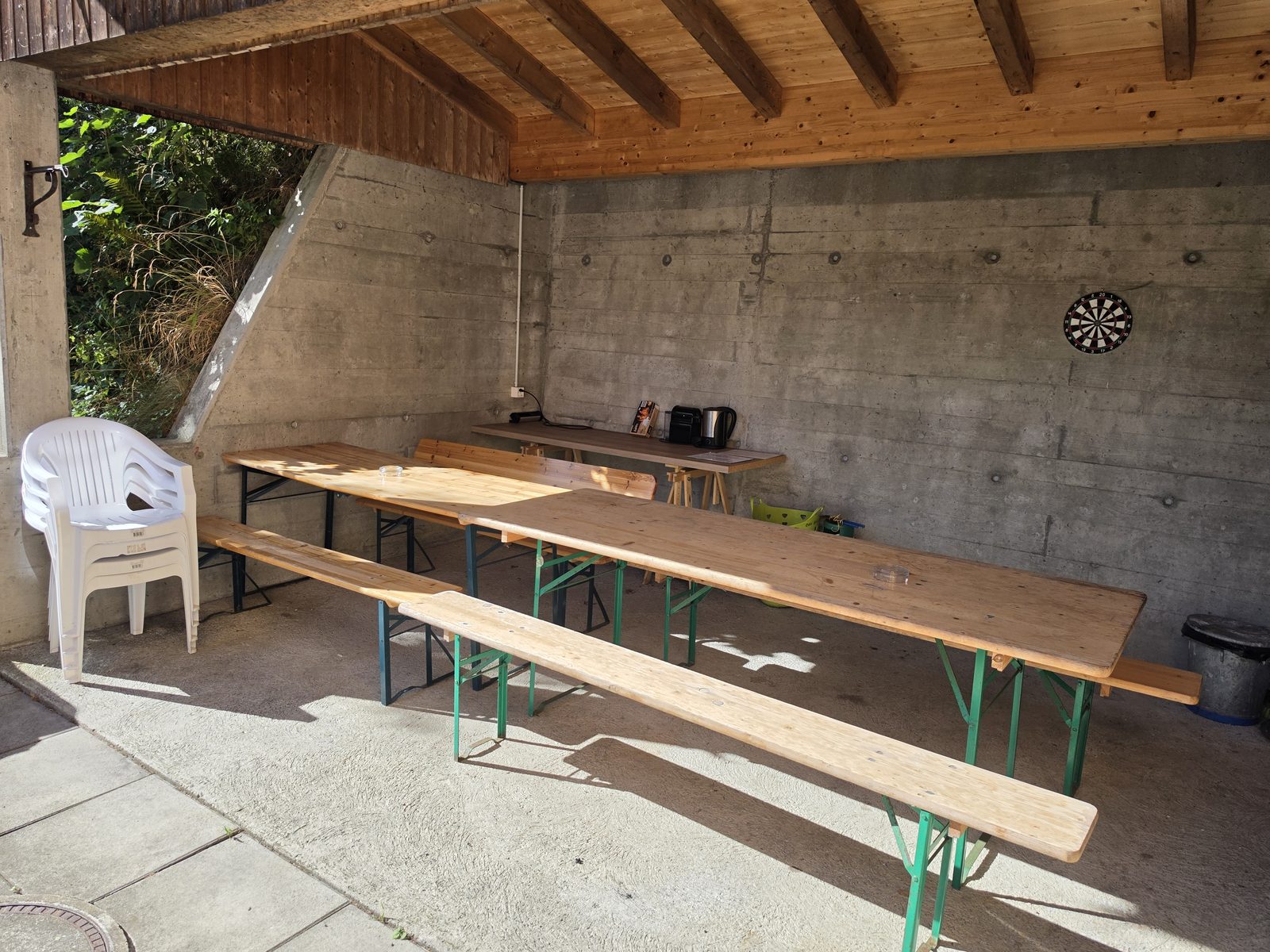 Überdachter Sitzplatz mit langen Tischen, Bänken und Dartscheibe im wettergeschützten Bereich (Pergola)